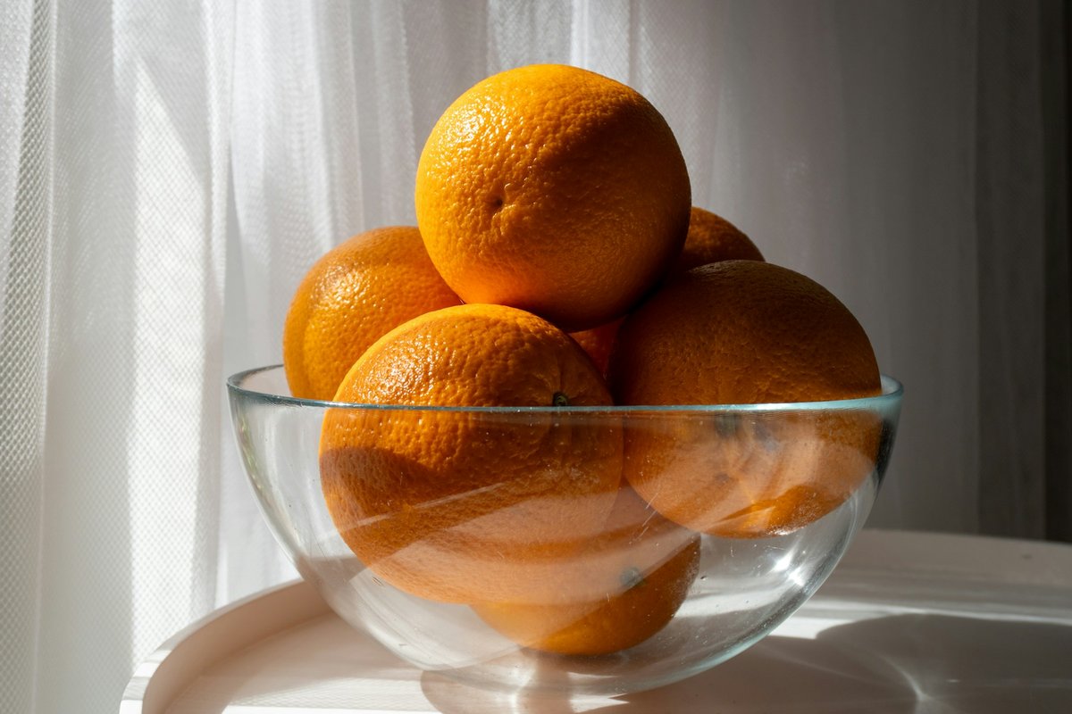 Oranges dans un bol de verre devant un voilage