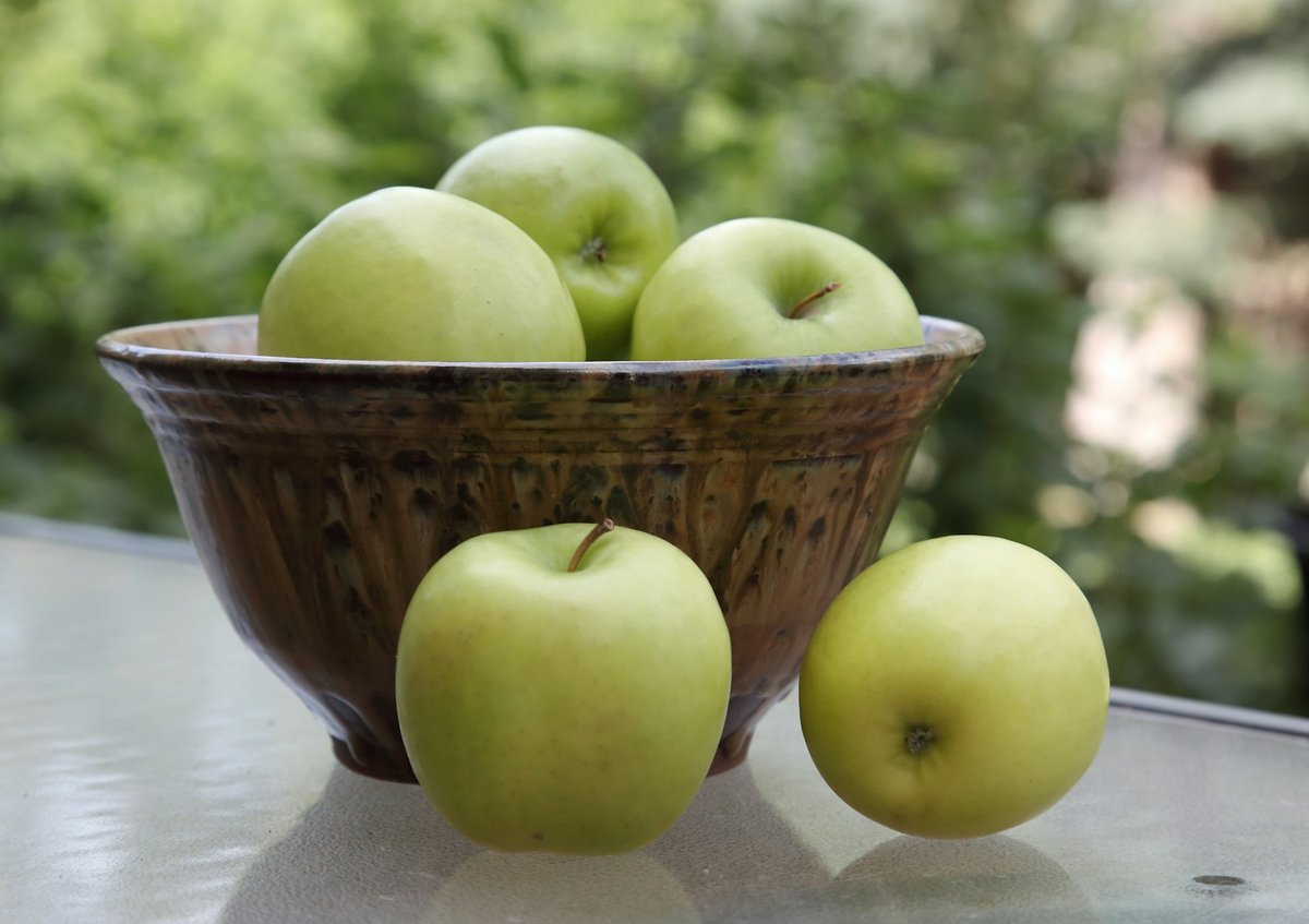 Pommes vertes dans un bol en céramique, jardin à l'arrière-plan